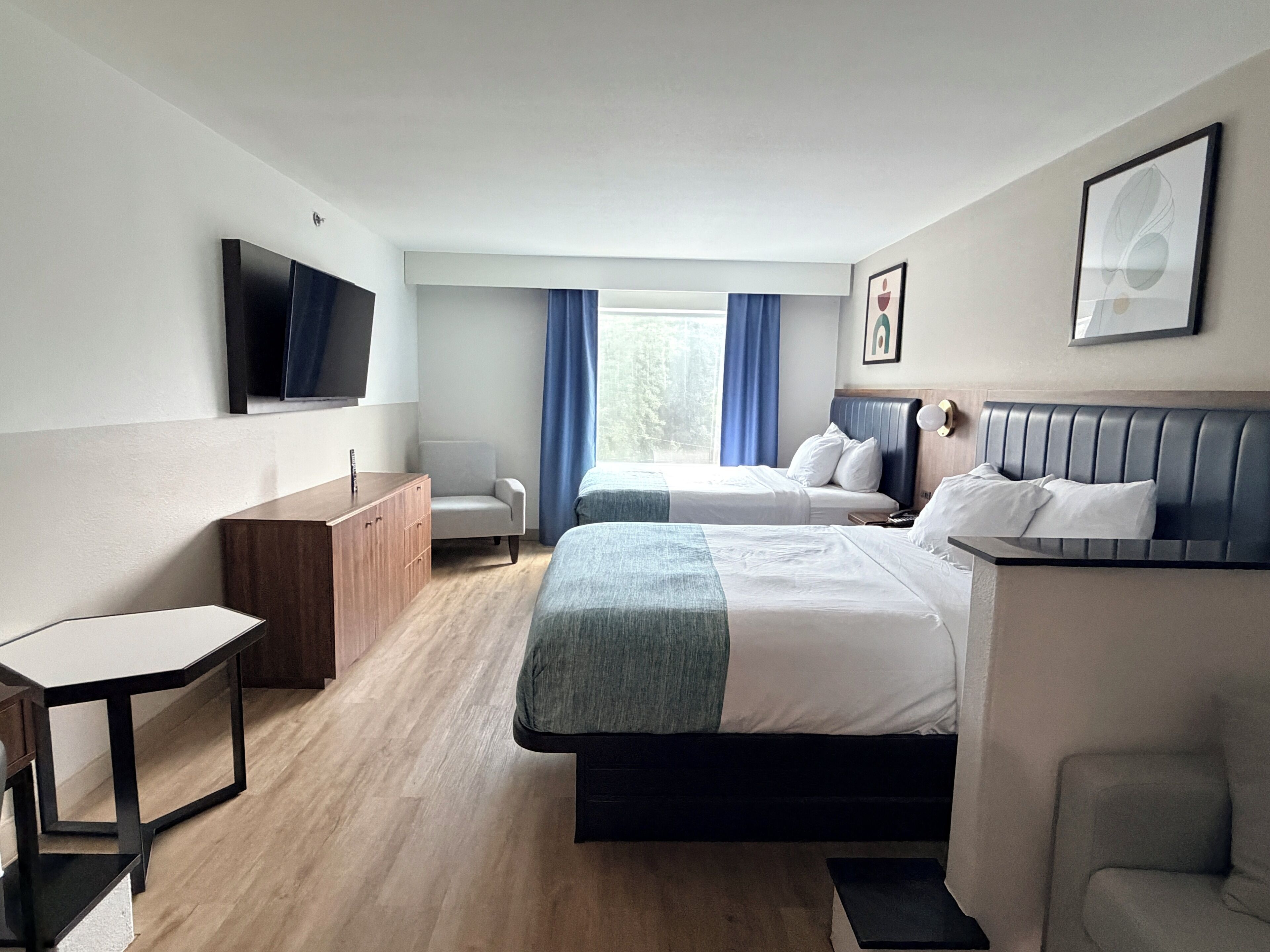 A hotel room with two beds, a desk, a chair, a TV, and a window with curtains.