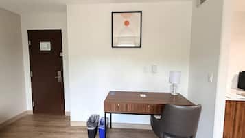 A room with a wooden desk, a chair, a trash bin, and a framed picture on the wall.