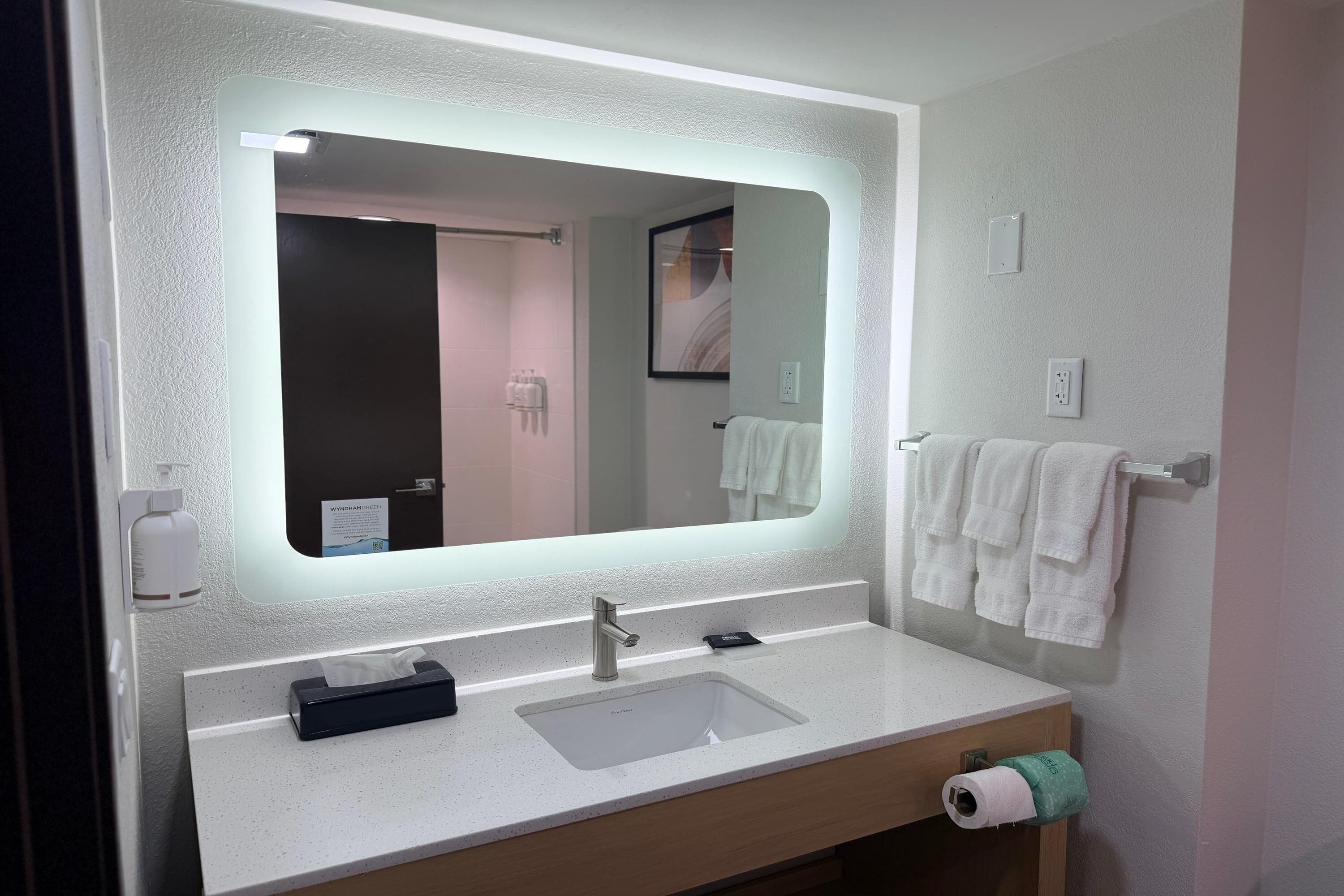 Ein Badezimmer mit einem großen Spiegel, einem Waschbecken, einem Handtuchhalter und einem Toilettenpapierhalter.