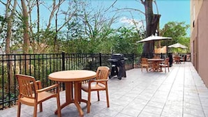 An outdoor patio with a round table and chairs, a grill, and umbrellas.