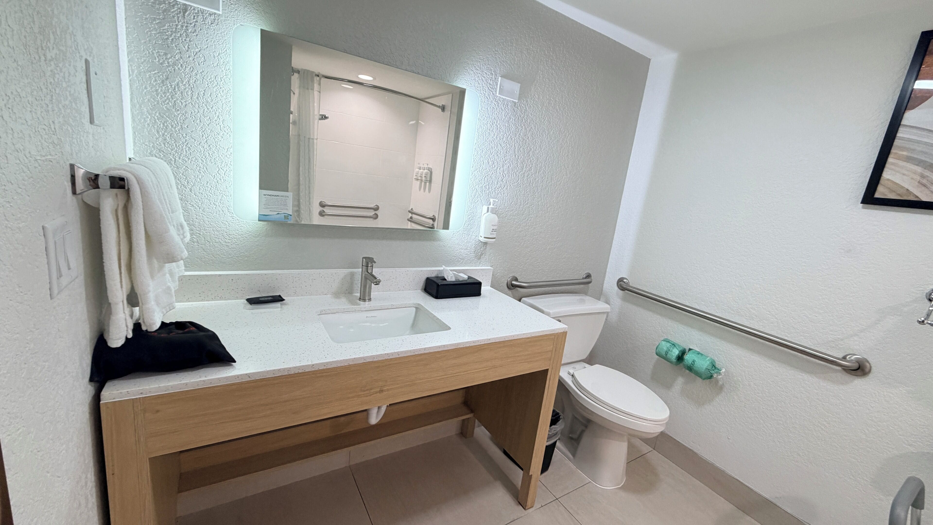 A modern bathroom with a wooden vanity, a sink, a toilet, and a handrail.