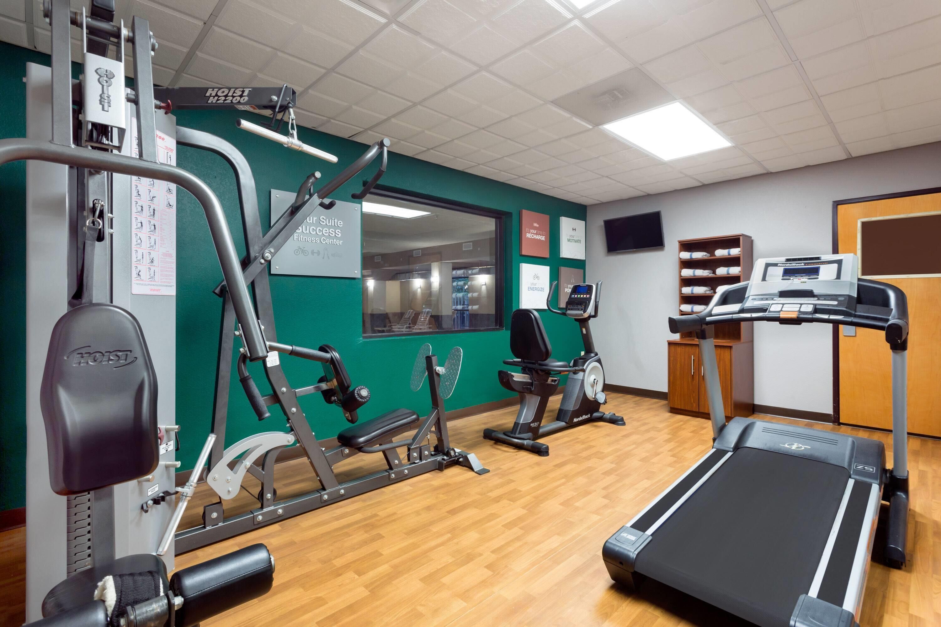 Un gimnasio con equipo de ejercicio, cinta de correr y carteles motivacionales en las paredes.