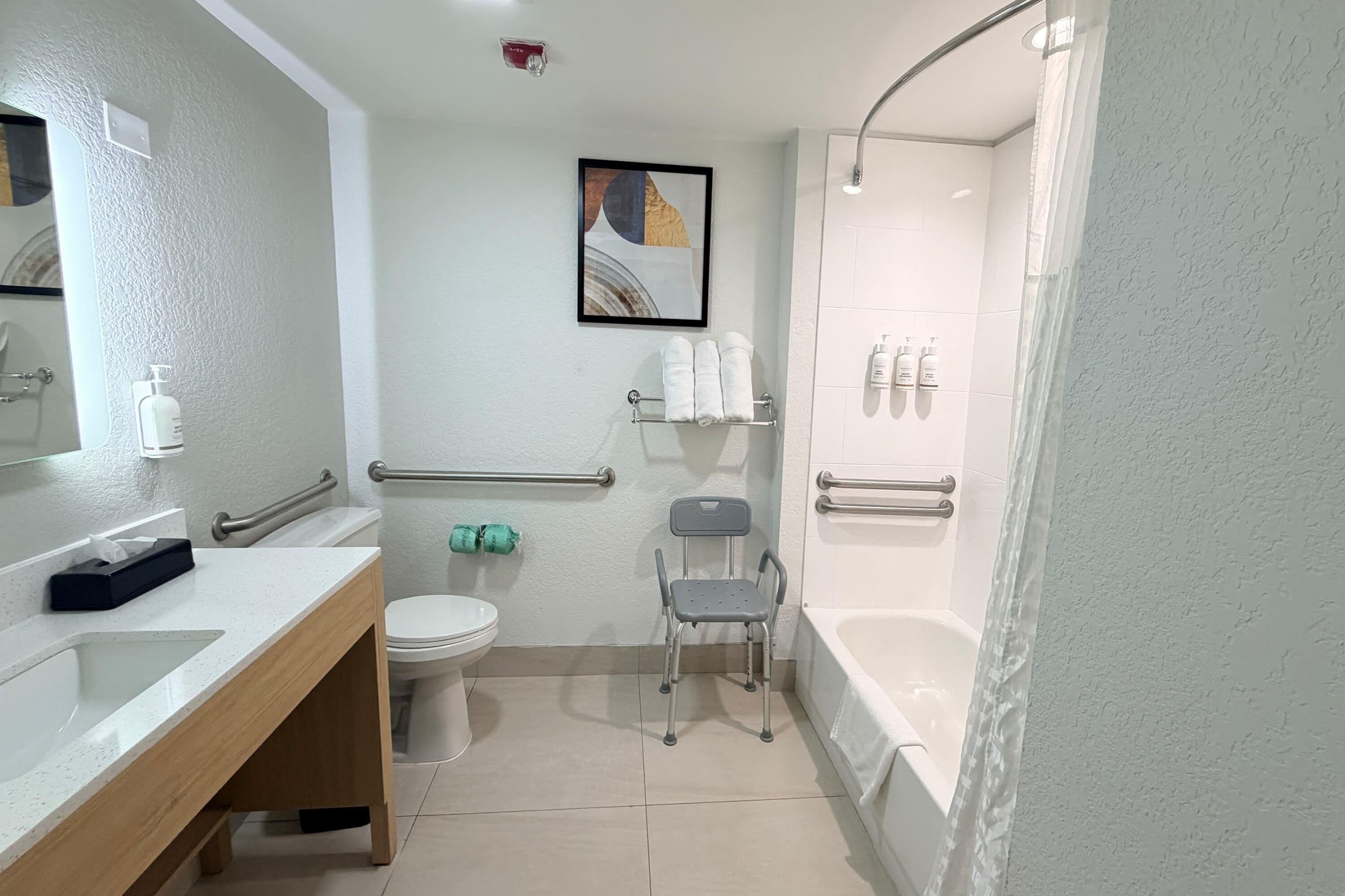 Un baño moderno con inodoro, lavamanos, ducha y una silla accesible para sillas de ruedas.