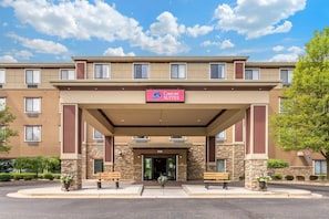 A hotel entrance with a sign reading 'Comfort Suites,' a covered entrance, and stone pillars.