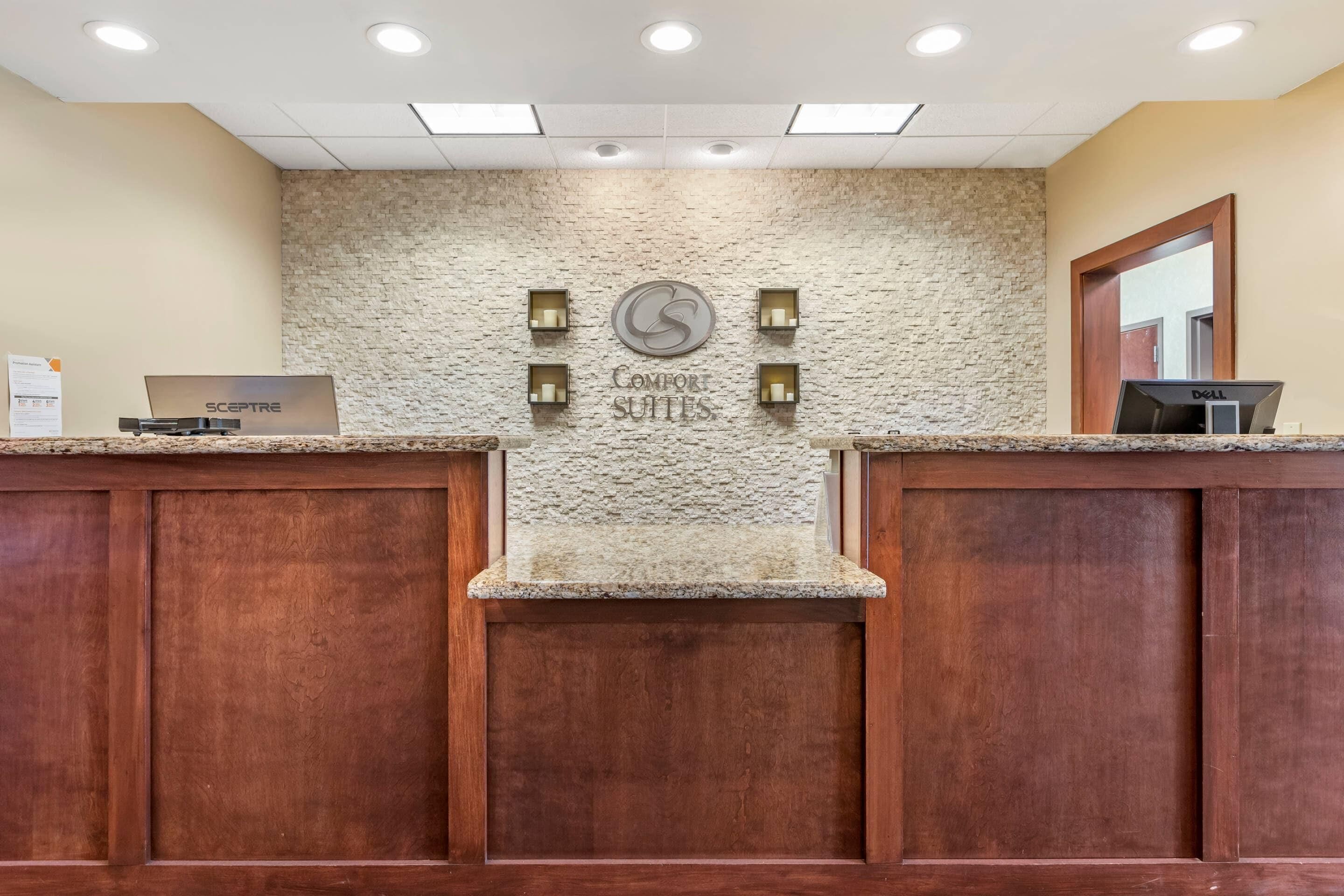 A reception area with a stone wall, a sign reading 'Comfor Suites,' and two computer monitors on the counter.
