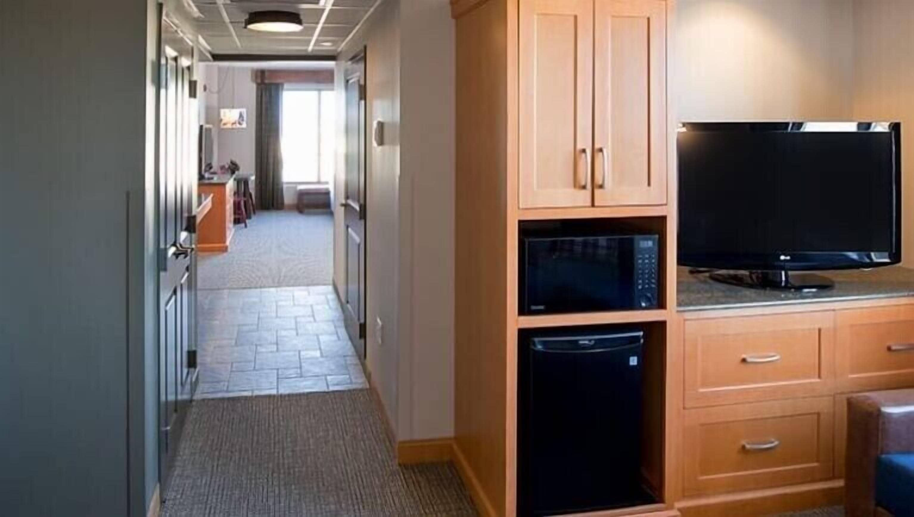 A hotel room with a kitchenette, a microwave, a dishwasher, and a flat-screen TV.