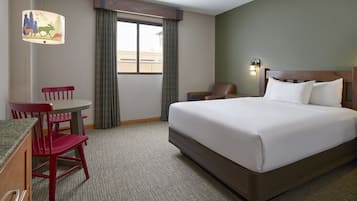 A hotel room with a bed, a desk with a chair, a window with curtains, and a lamp with a forest scene.