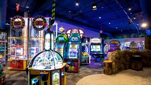Une salle d’arcade intérieure proposant divers jeux, notamment des jeux d’adresse avec des pinces et des jeux de course.