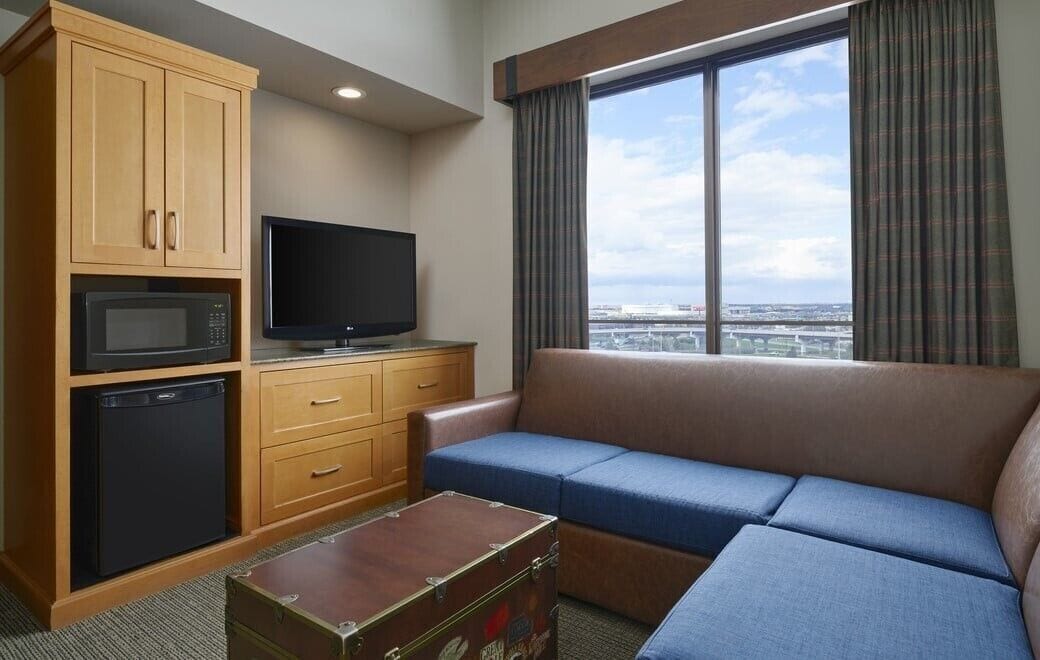 A hotel room with a sofa, a television, a microwave, and a small refrigerator.