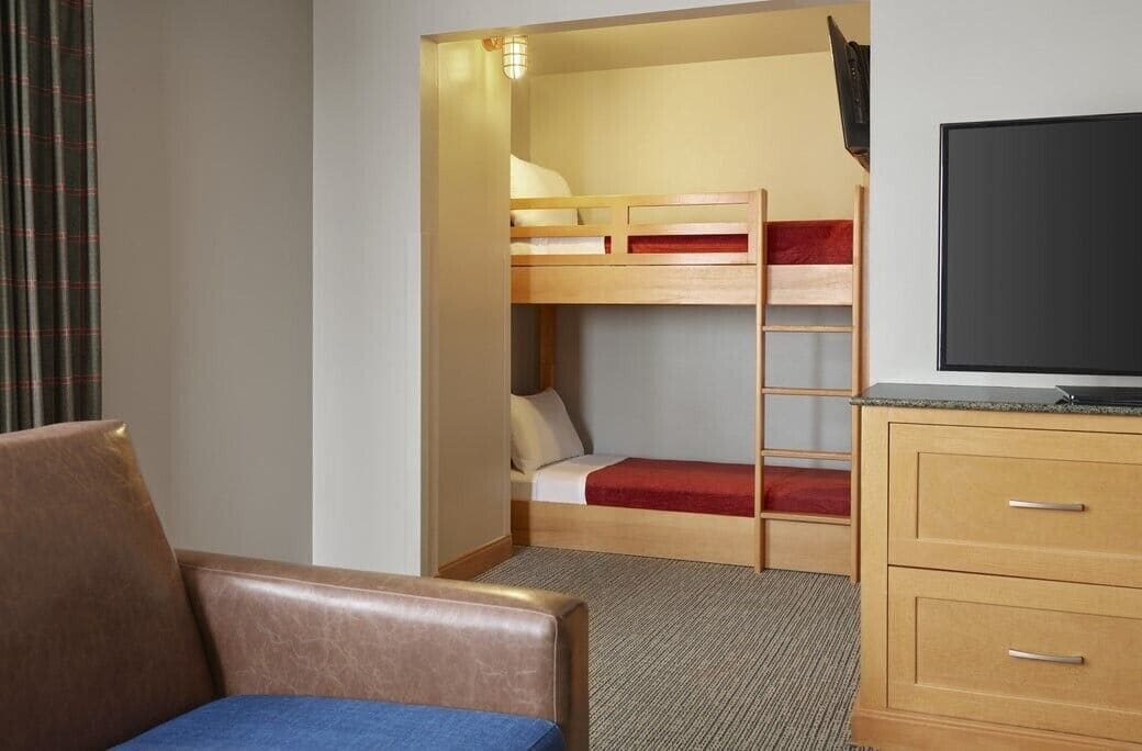 A hotel room with a bunk bed, a television, a desk, and a chair.