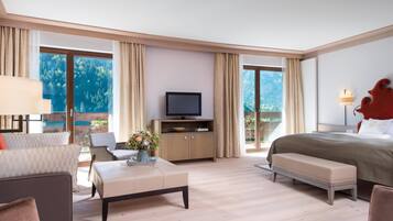 A modern hotel room with a large bed, a TV, a sofa, a coffee table, and a view of the mountains.