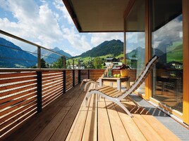 Terraza de madera con barandilla de vidrio que da a un paisaje montañoso.