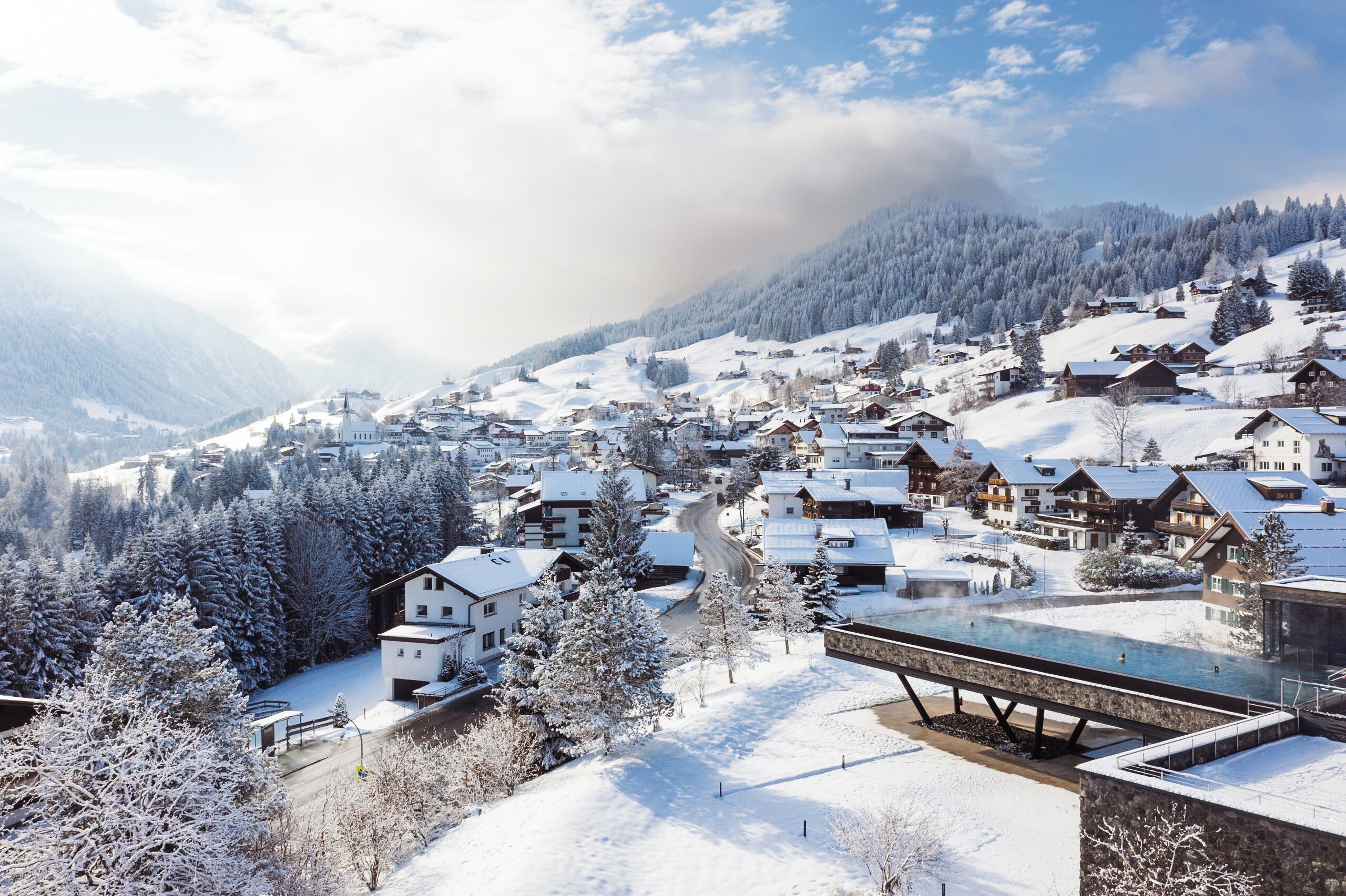 A snow-covered village with traditional wooden houses, a river, and a mountain backdrop.