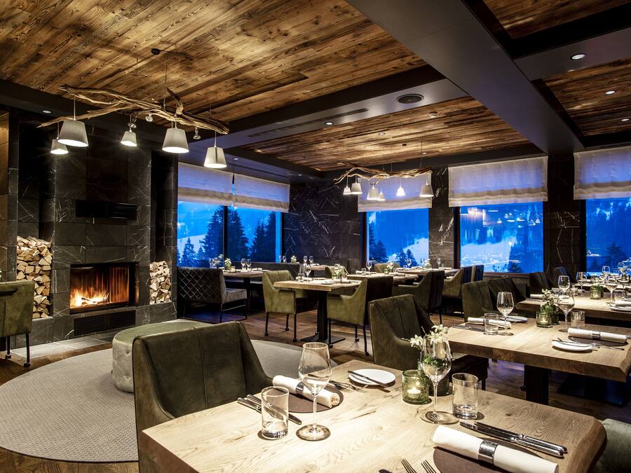 Ein Restaurant mit Kamin, Holzbalkendecke und großen Fenstern mit Blick auf Bäume.