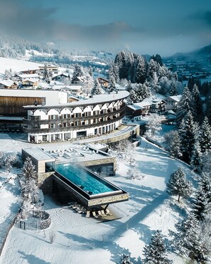 A snow-covered resort with a pool area, modern buildings, and a mountainous backdrop. - A-ROSA Ifen Hotel Kleinwalsertal (Mittelberg)