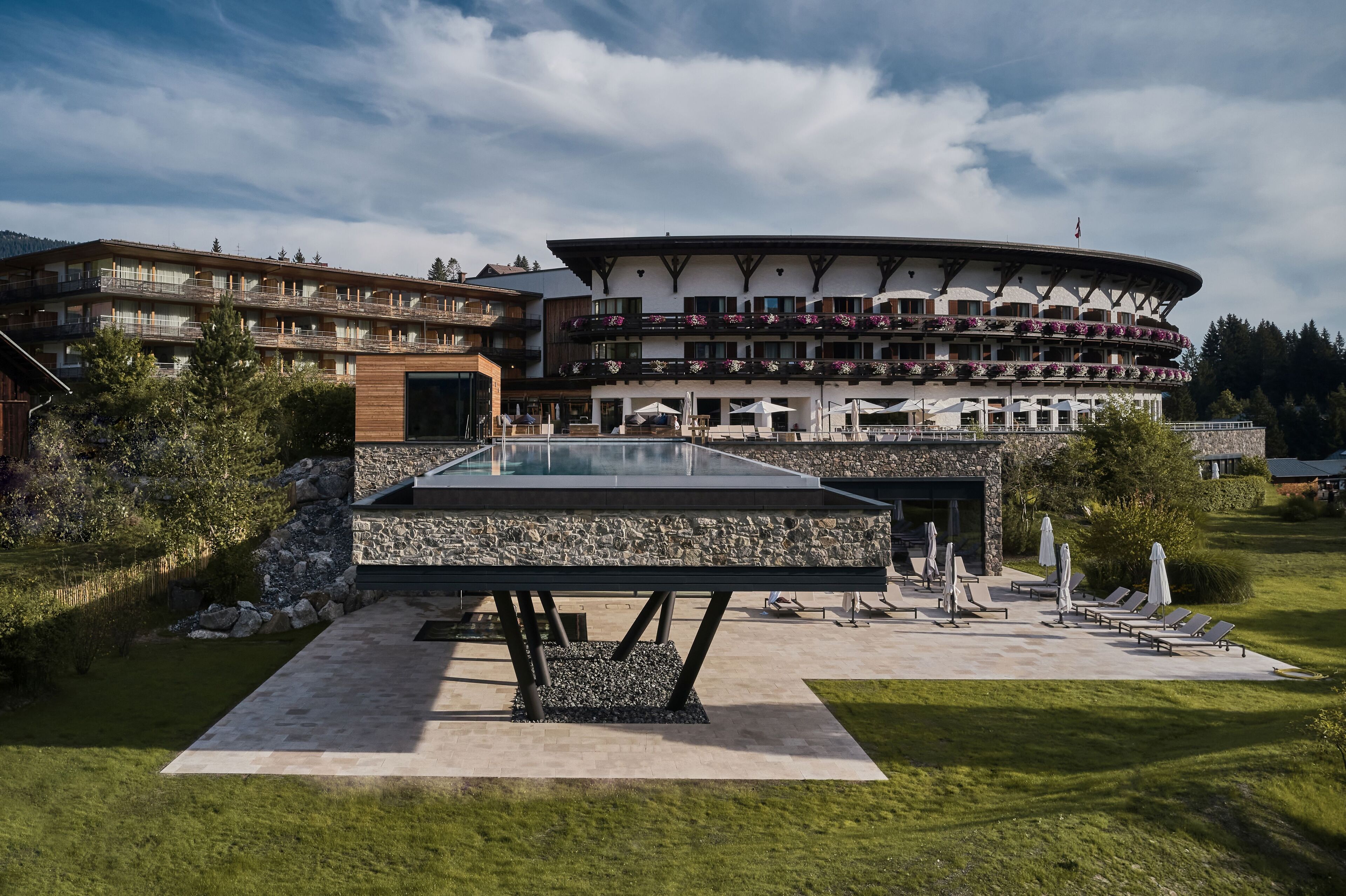 Ein modernes Hotel mit Poolbereich, Außenbereich zum Sitzen und einer malerischen Bergkulisse.