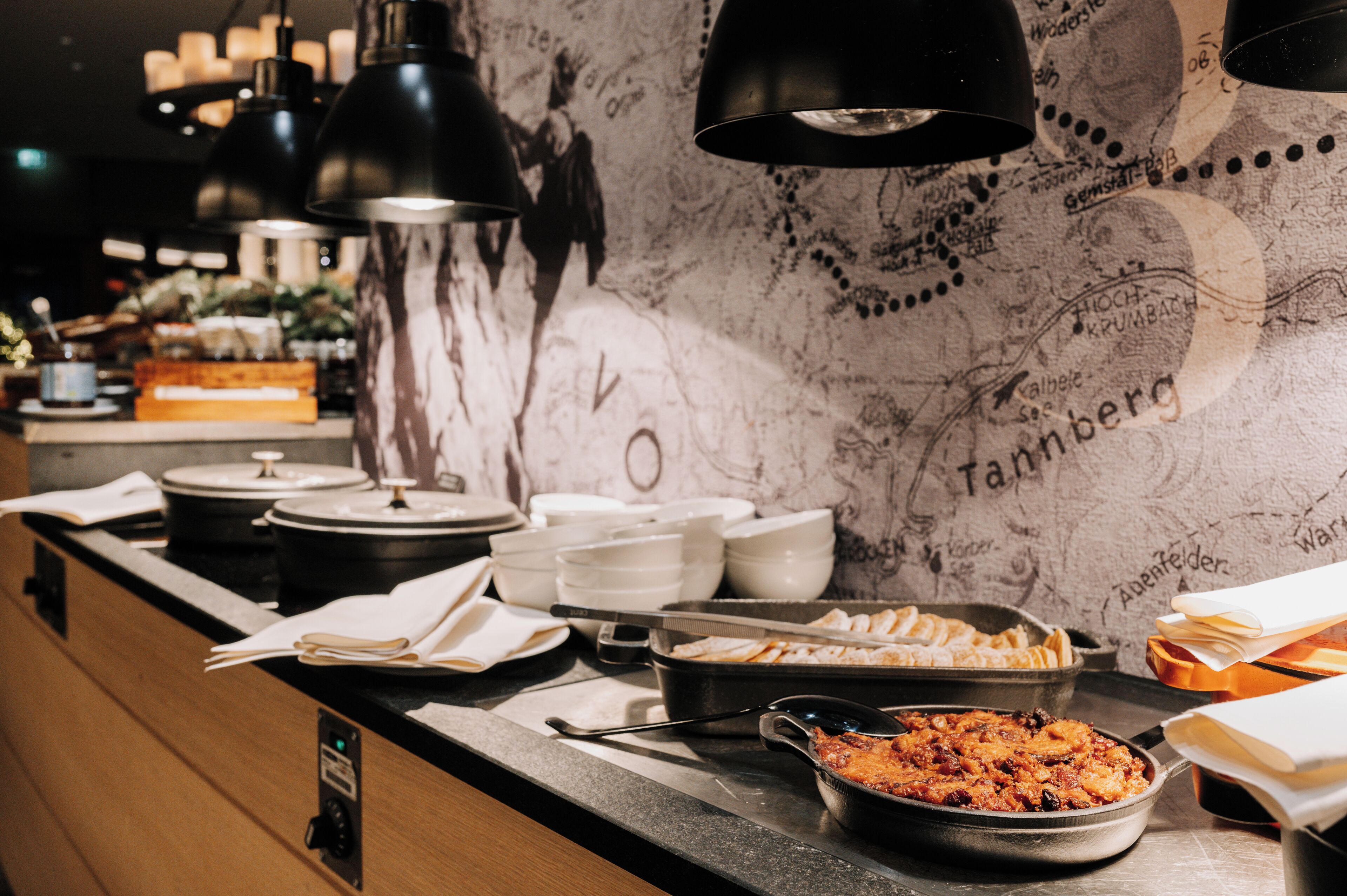 A buffet setup with various dishes, serving utensils, and a marble wall with text.