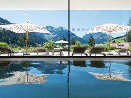 Zona junto a la piscina con sillas de descanso y sombrillas, con vistas a un paisaje montañoso.