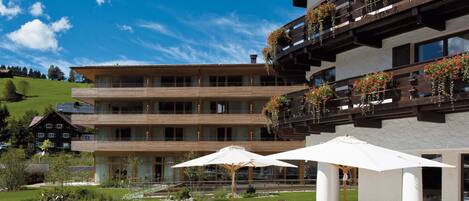 A hotel with outdoor seating, a terrace, and a view of a green hillside.