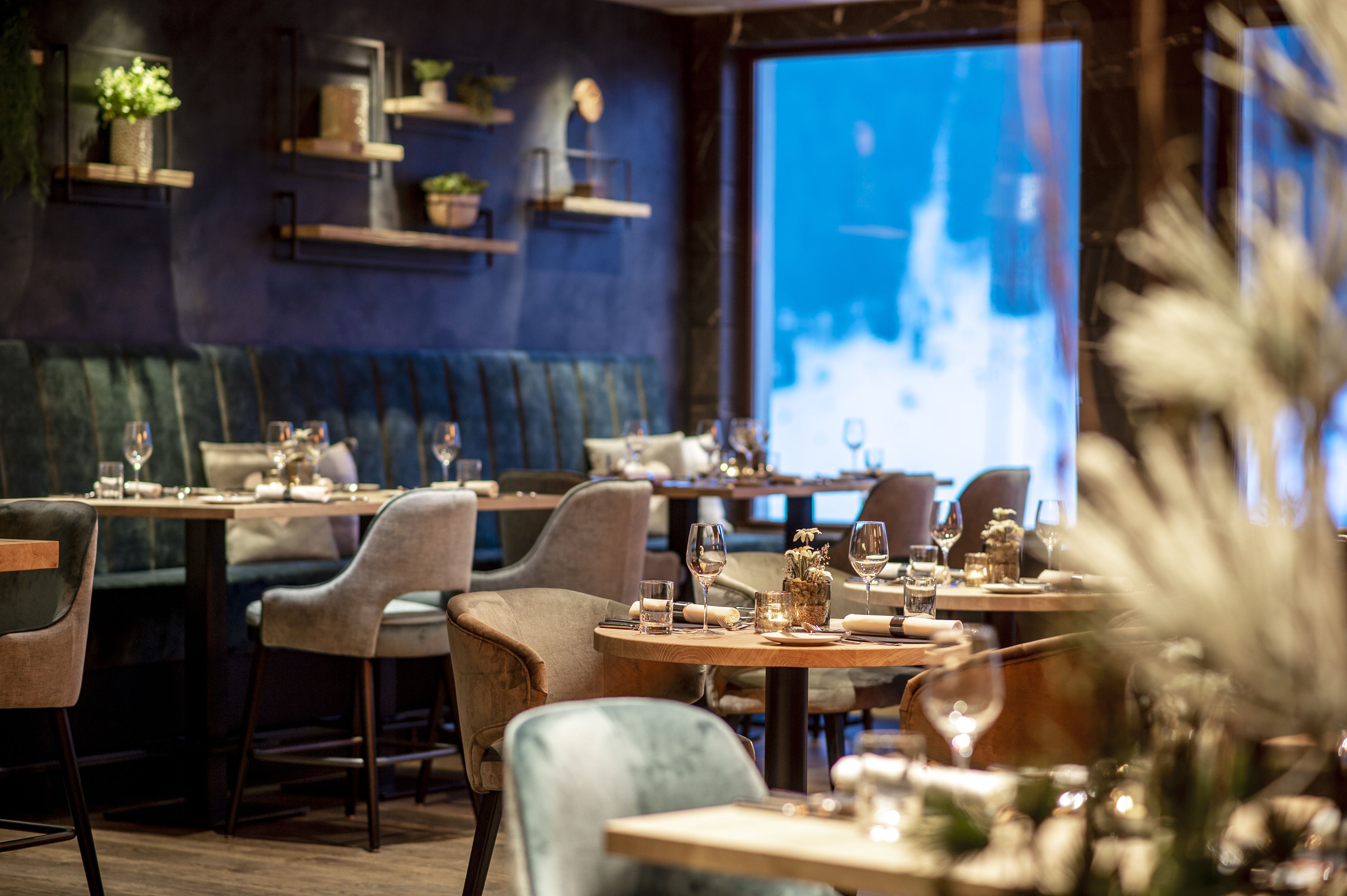 Un restaurante con mesas redondas, cabinas acolchadas y estanterías con plantas.