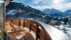Une terrasse en bois dotée d’une balustrade en verre, offrant une vue sur un paysage montagneux enneigé.