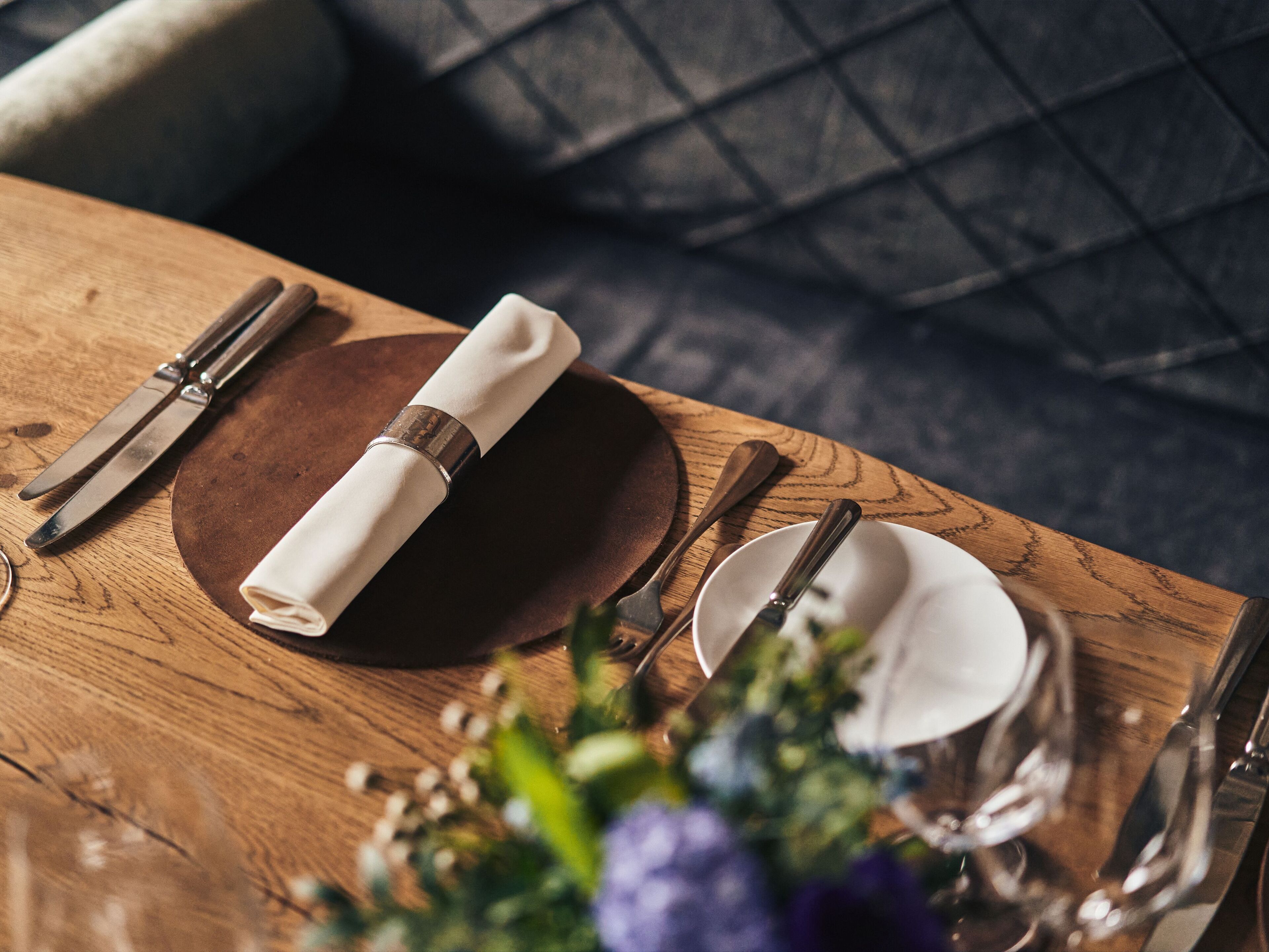 Een houten tafel gedekt met bestek, een gevouwen servet en een bord.