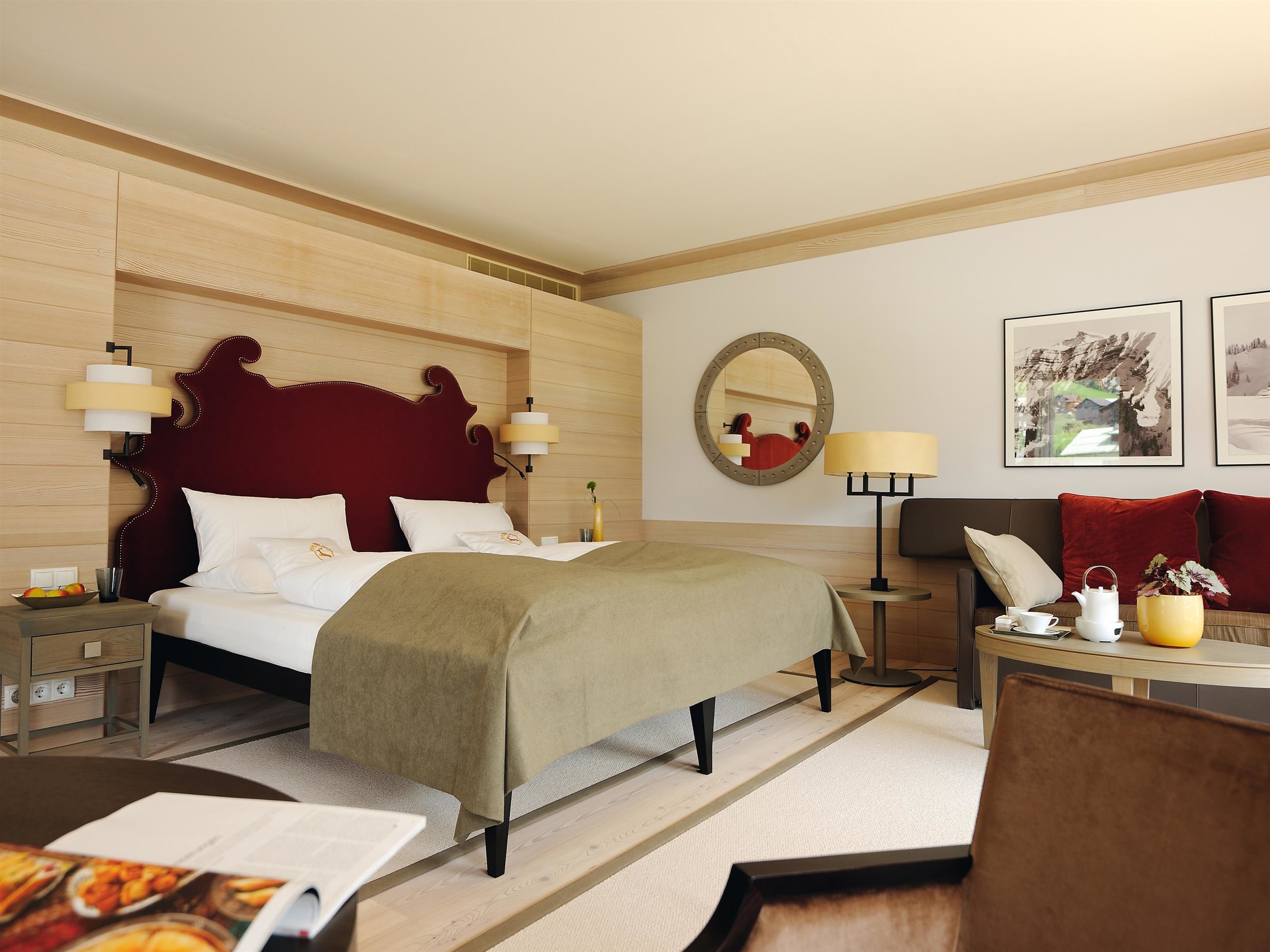 A hotel room with a large bed, bedside tables, a sofa, a coffee table, a mirror, and framed pictures on the wall.