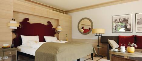 A hotel room with a large bed, bedside tables, a sofa, a coffee table, a mirror, and framed pictures on the wall.