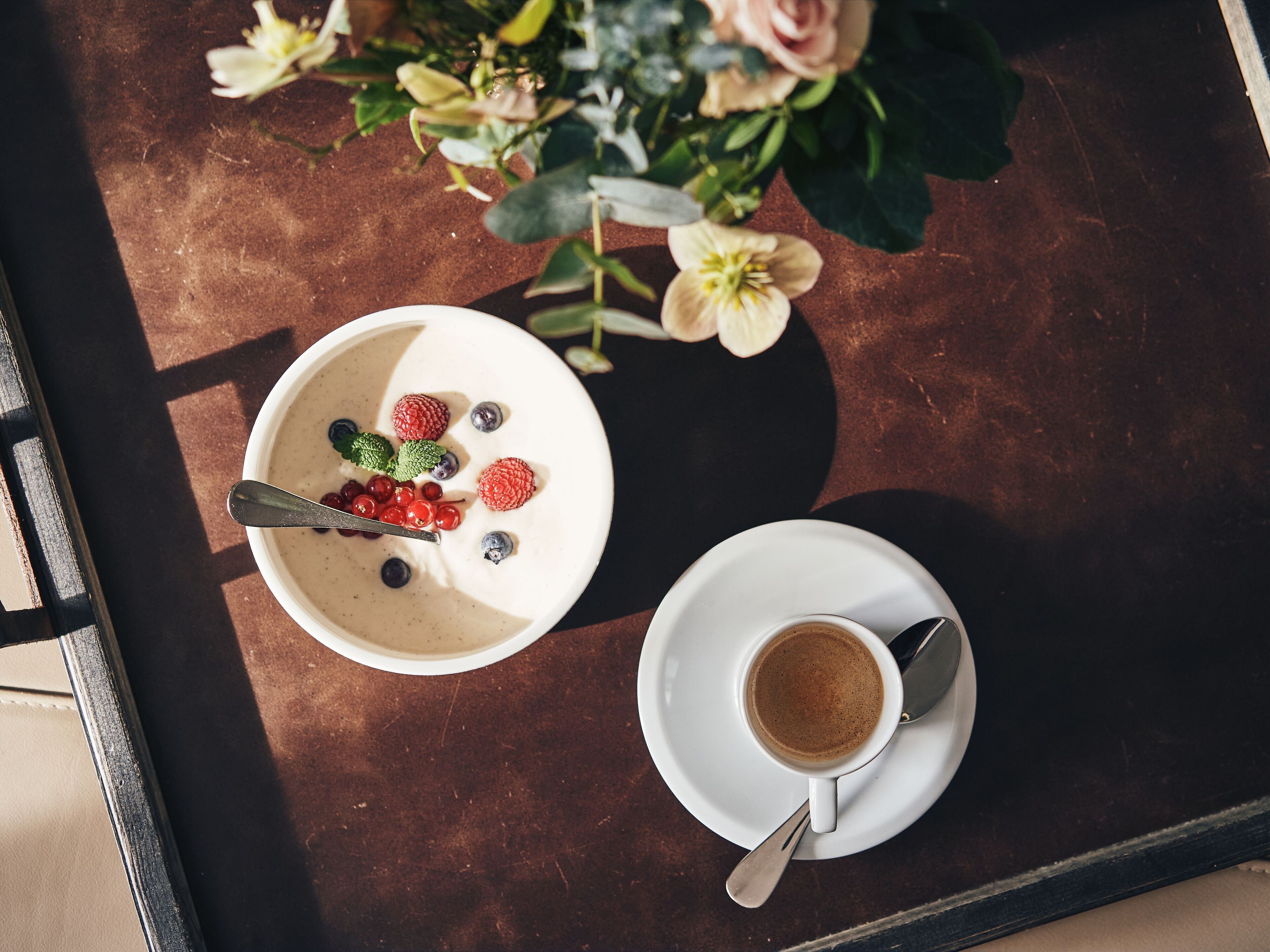 A table with a bowl of yogurt topped with berries and a cup of coffee.