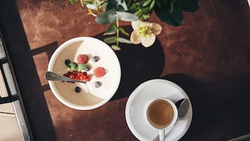Uma mesa com iogurte coberto de frutas vermelhas e uma xícara de café.