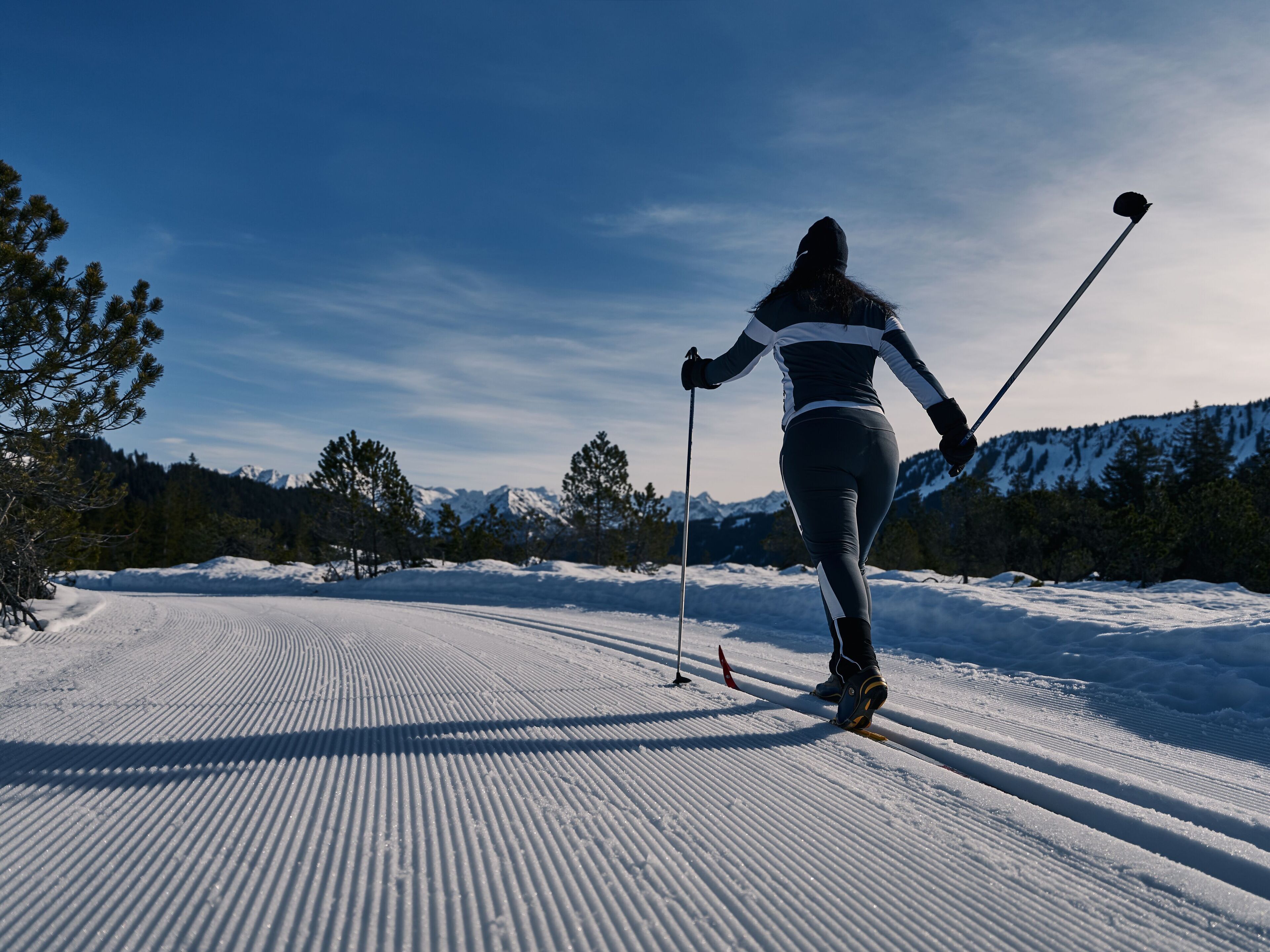 Une personne fait du ski sur une piste damée, avec des montagnes enneigées en arrière-plan.