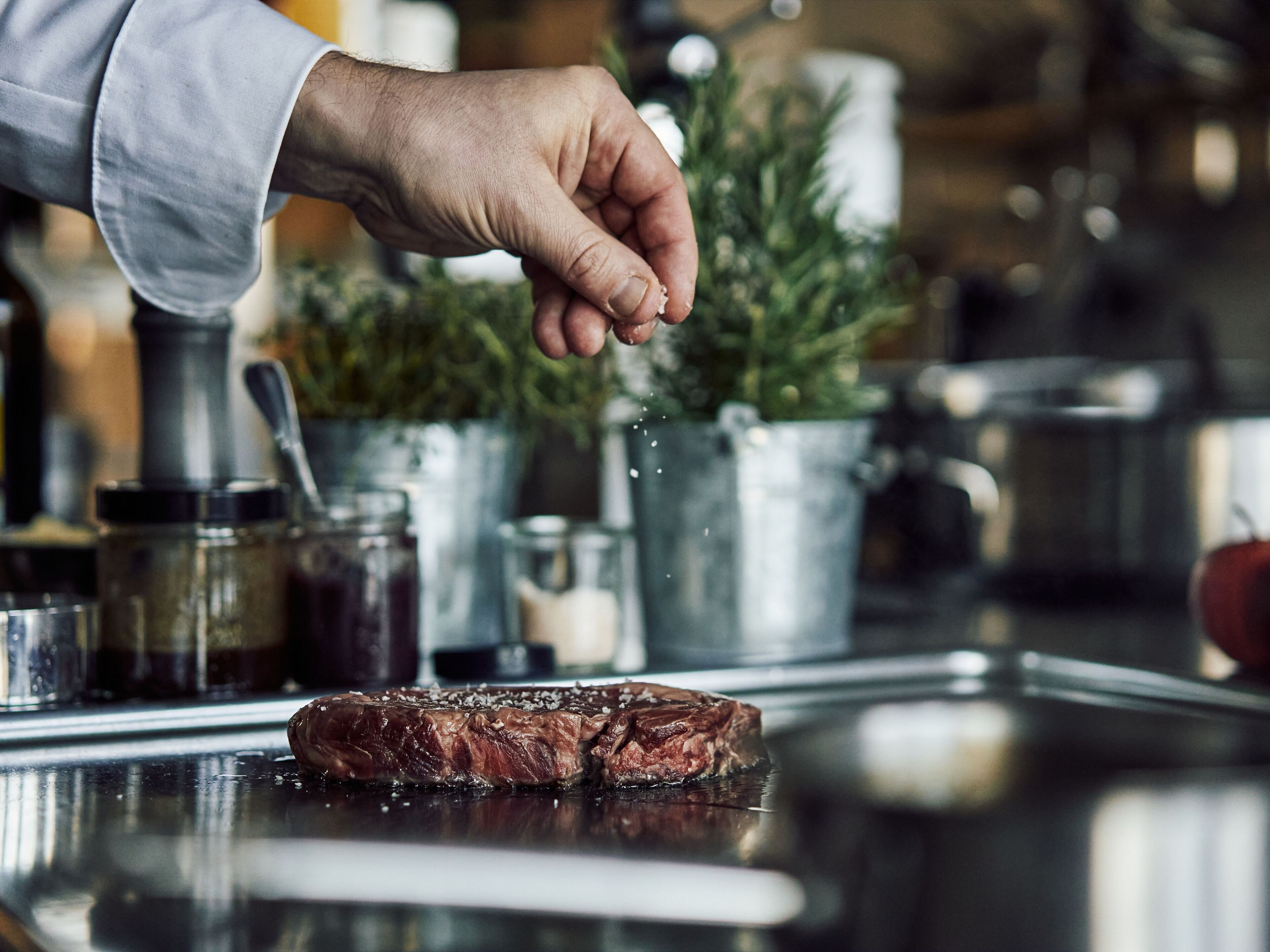 Ein Koch würzt ein Steak mit Kräutern.