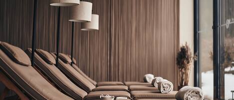 A spa room with multiple massage chairs, a wooden bench, and a window with a view of the outdoors.