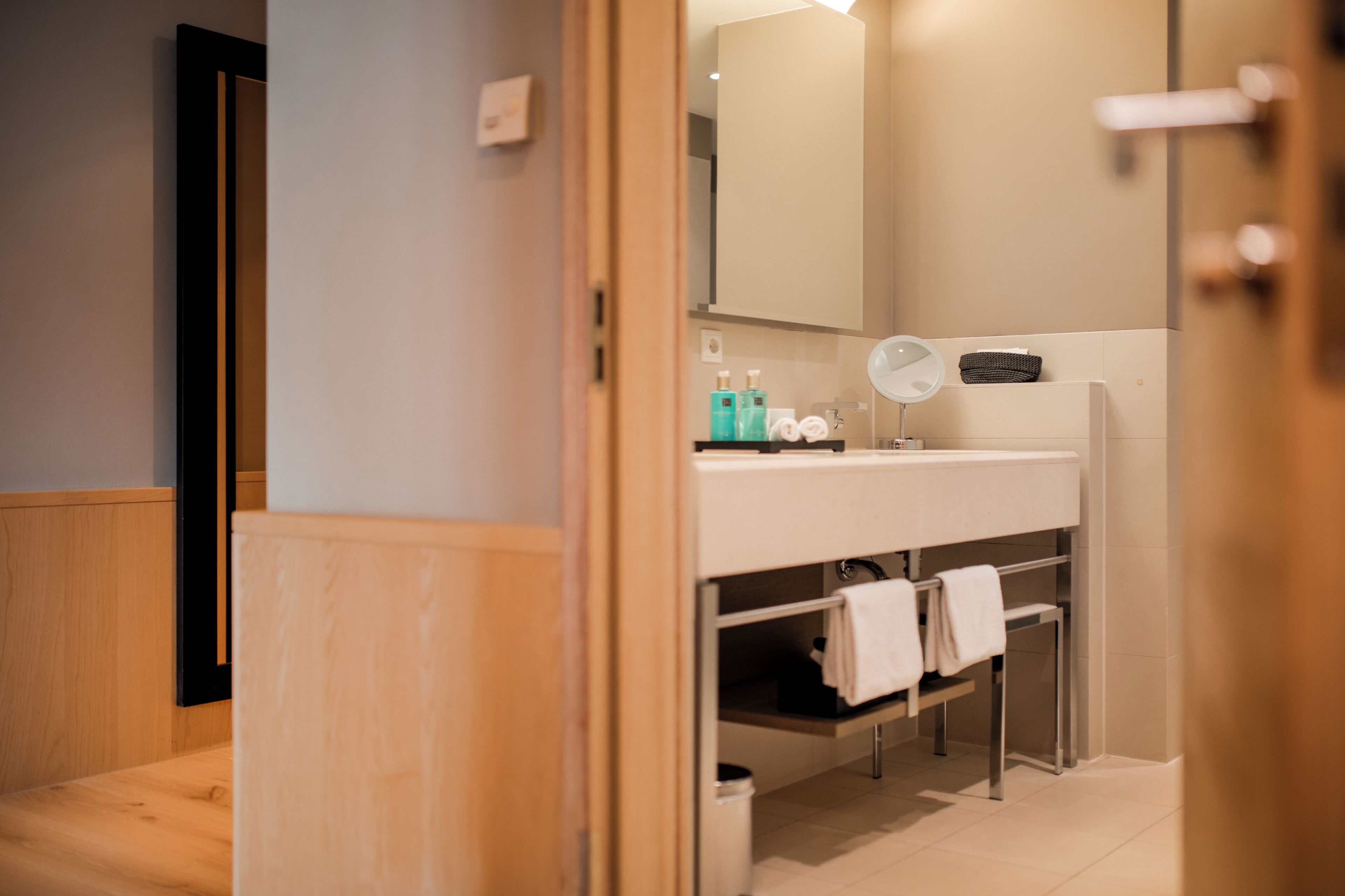 Un baño moderno con suelo de madera, un lavabo blanco con espejo y un perchero para toallas.
