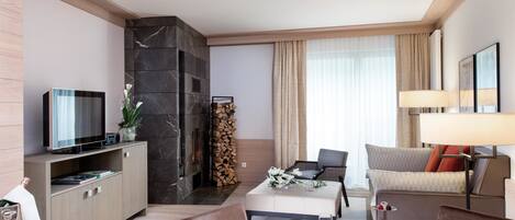 A modern hotel room with a flat-screen TV, a fireplace, a dining area with a table set for two, and a sofa.
