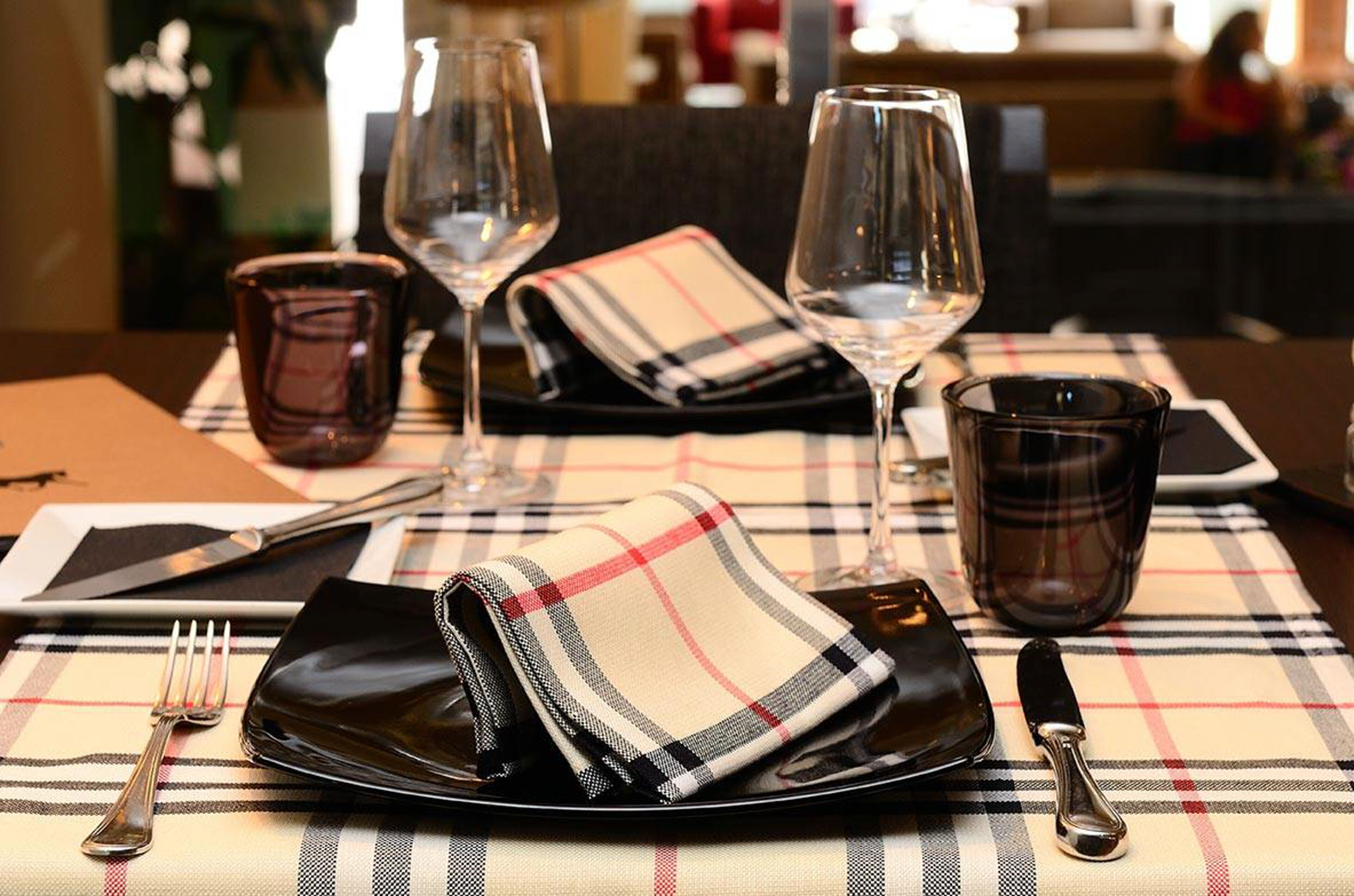 A dining table set with a plaid tablecloth, wine glasses, a glass of water, cutlery, and a folded napkin.