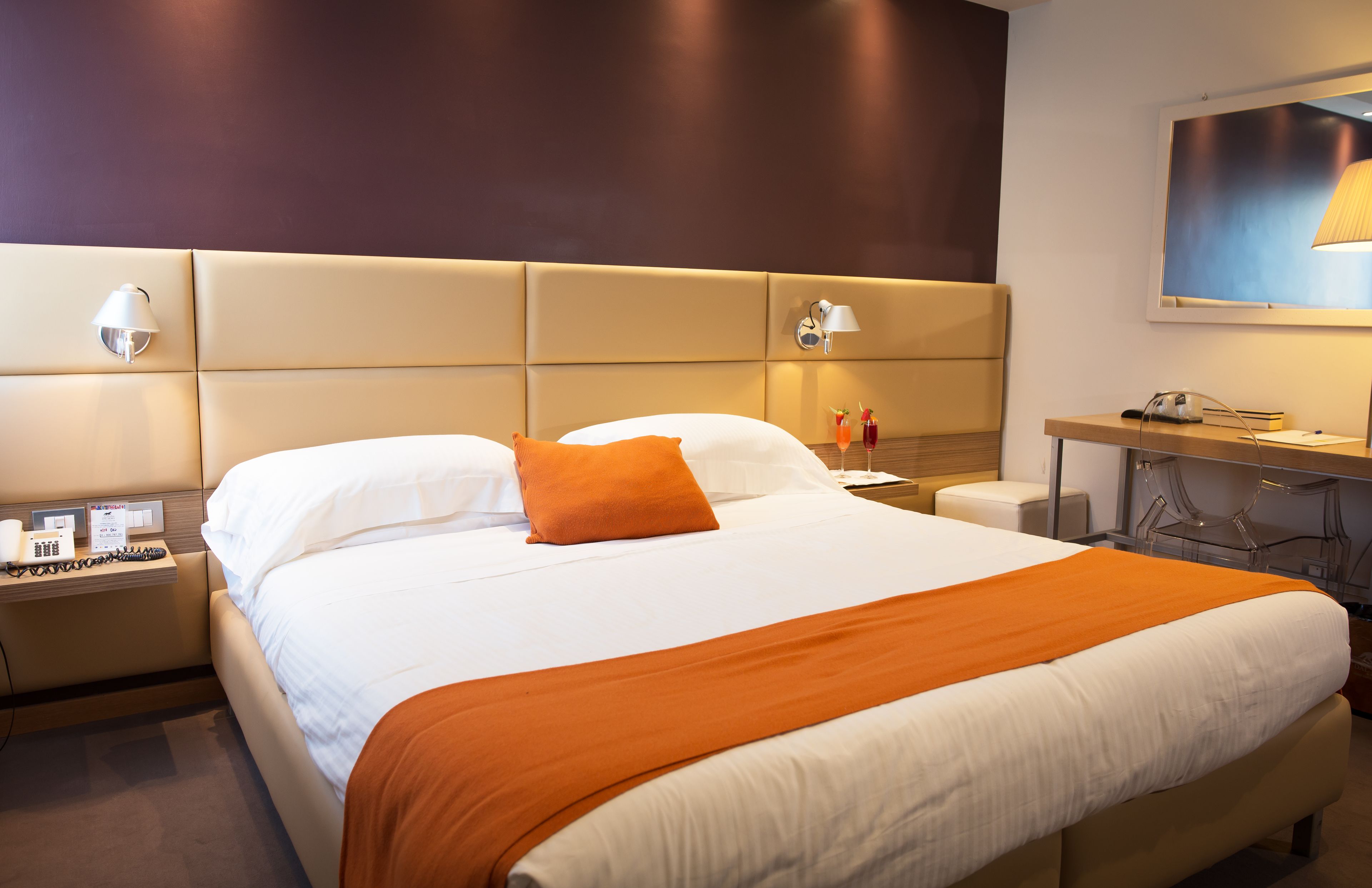 A hotel room with a large bed, two bedside lamps, a desk with a lamp, and a wall-mounted picture.