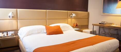 A hotel room with a large bed, two bedside lamps, a desk with a lamp, and a wall-mounted picture.