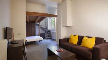 A modern living room with a brown sofa, a coffee table, and a TV on a wooden desk. A staircase leads to an upper level.