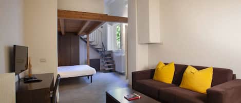 Una sala de estar moderna con un sofá marrón, una mesita de centro y un televisor sobre un escritorio de madera. Una escalera conduce a un nivel superior.