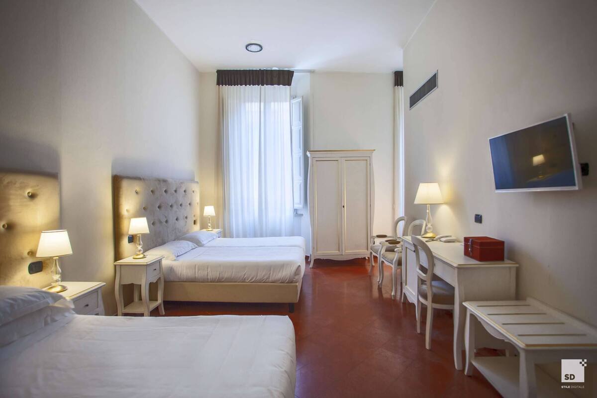 Ein Hotelzimmer mit zwei Betten, einem Schreibtisch, einem Sessel, einem Fernseher und einem Kleiderschrank.
