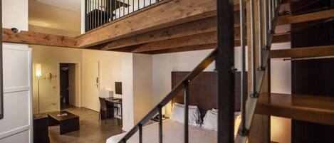 A modern hotel room with a wooden staircase, a bed, a desk, and a small seating area.