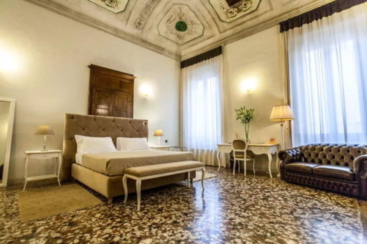 Ein Hotelzimmer mit Bett, einer Bank, einem Schreibtisch, einem Sessel, einer Couch und einer dekorativen Decke.