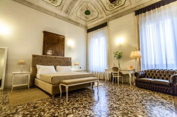 A hotel room with a bed, a bench, a desk, a chair, a sofa, and a decorative ceiling.