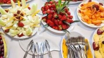 Una mesa con fuentes de fruta variada, platos, utensilios y pilas de platos.