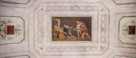 A ceiling with a central fresco surrounded by ornate moldings and decorative elements.