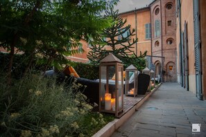 A pathway lined with lanterns and a tree, leading to a building with arched windows and a brick facade.