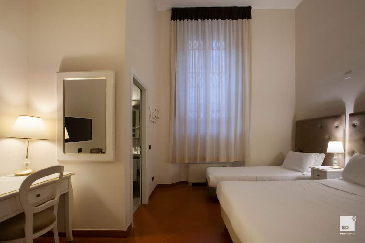 Ein Hotelzimmer mit Schreibtisch, zwei Betten, einem Spiegel und einem Fenster mit Vorhängen.