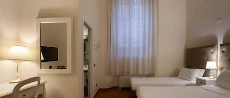 Quarto de hotel com escrivaninha, duas camas, espelho e janela com cortinas.