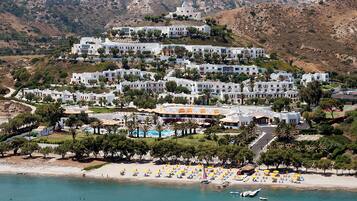 A coastal resort with multiple white buildings, a swimming pool, and a beach with umbrellas.
